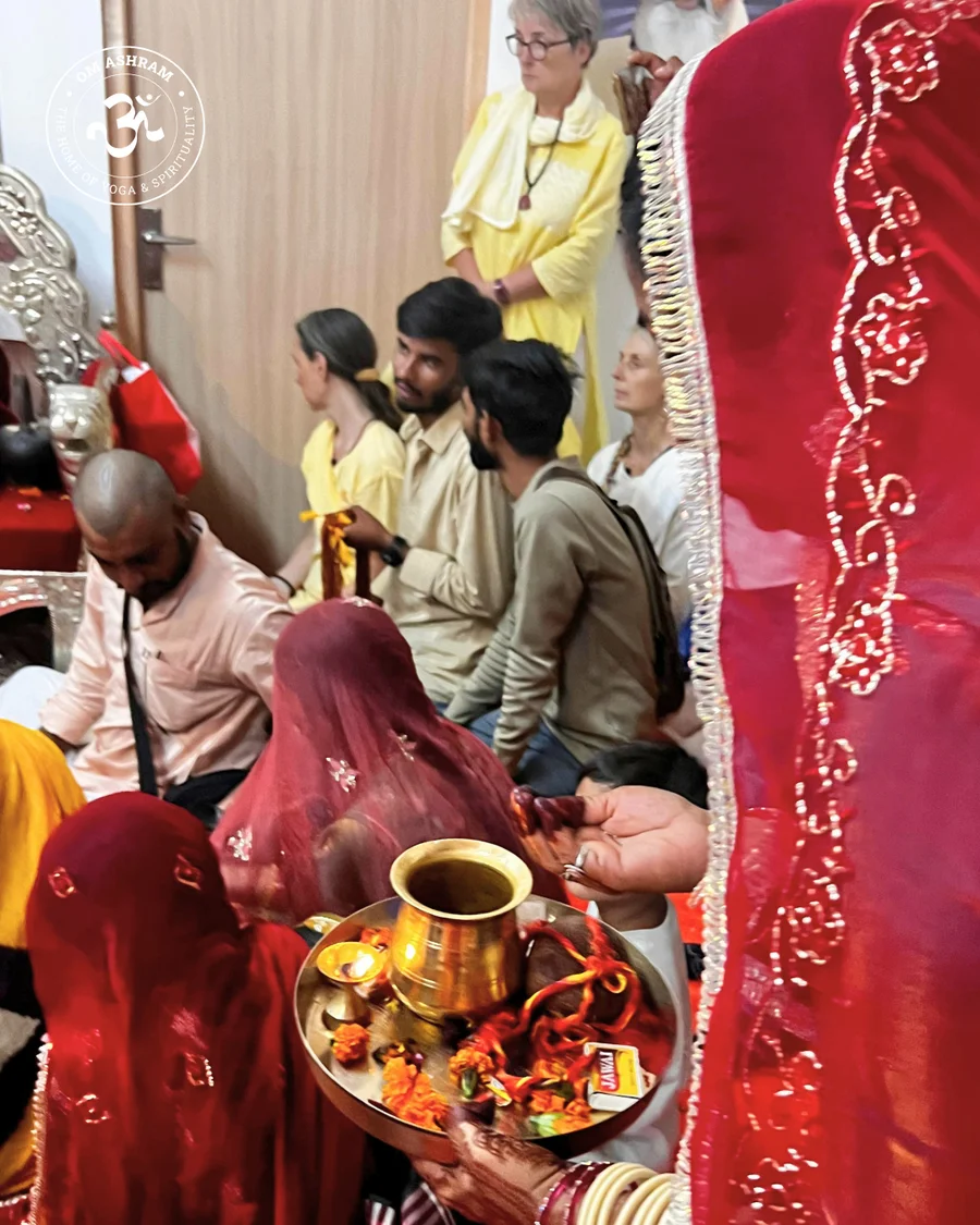  A woman in a saree carrying a puja thali with a lamp and holy water.